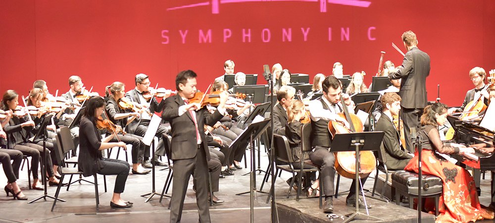 Symphony in C performing on stage against a red background with their logo projected