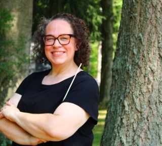 headshot of woman standing in front of trees and greenery