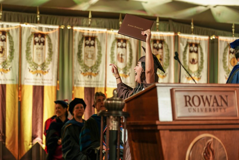 Graduate student walking across commencement stage with Rowan University degree holder in hand