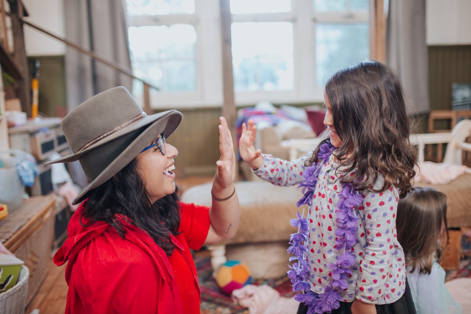 A mom and daughter dressed up in play costumes high-fiving in their living room