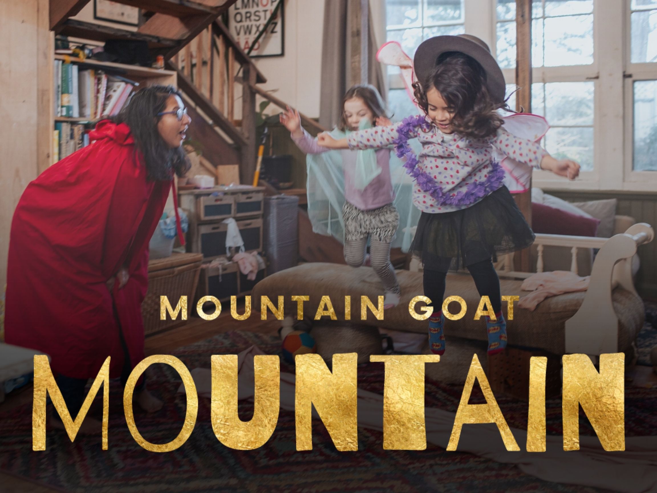 A mom and two kids dressed up and playing in their messy living room, with glitter title: Mountain Goat Mountain