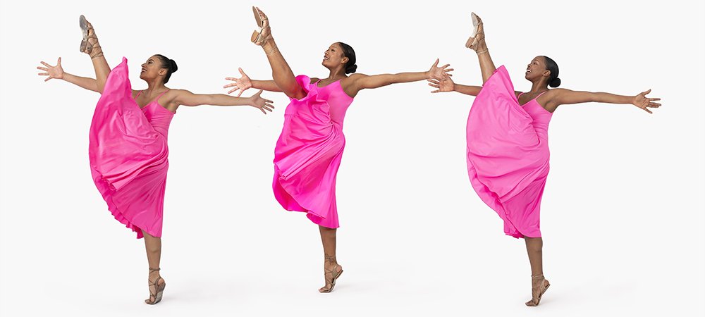 Three black female dancers in matching fuschia dresses against a white background, all arms outstretched, bodies facing right, with left legs extended high to the sky with pointed toes, standing on the balls of their right feet.