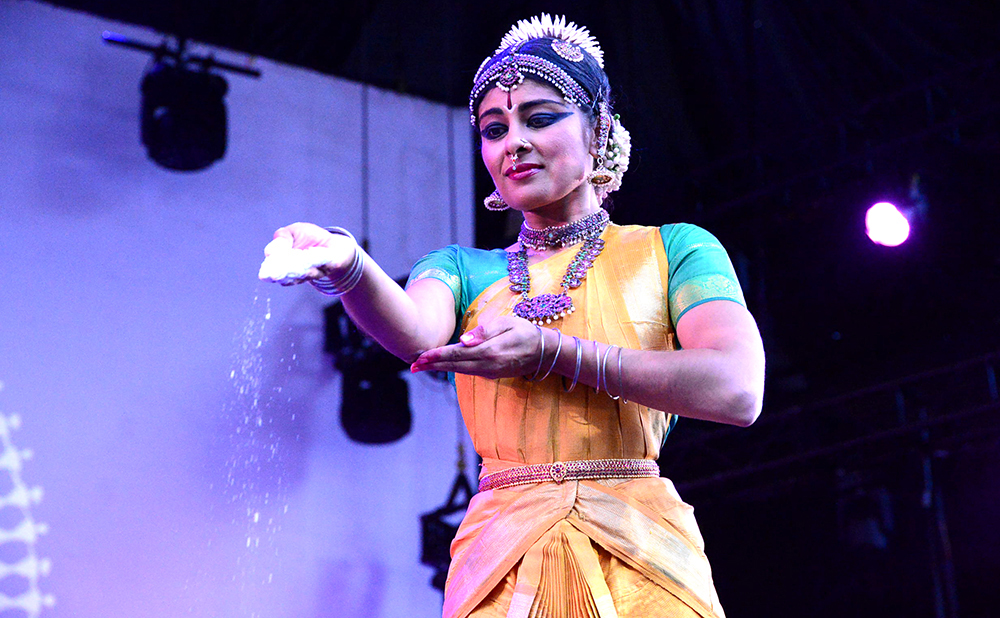 3. Close-up of a Bharatanatyam dancer in green releasing sacred sand from her palm.