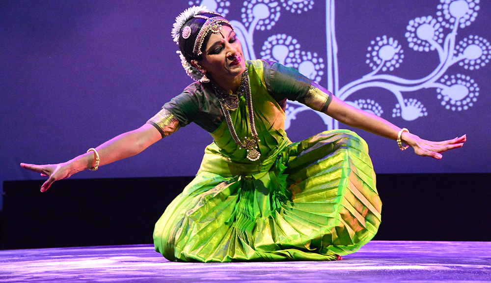 4. A seated Bharatnatyam dancer in bright green costume seated on the stage, bowing to the earth below.