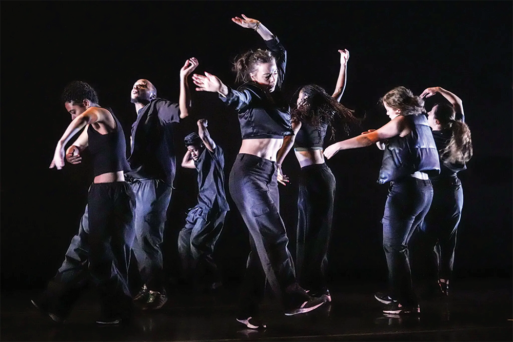 2. A cluster of 7 dancers in black pants, sneakers, vests, and crop tops, arms in all directions, bodies grooving.