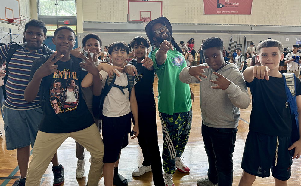 1. A Rennie Harris dancer in a crowded gymnasium, with 7 children, all pointing to the camera and posing.