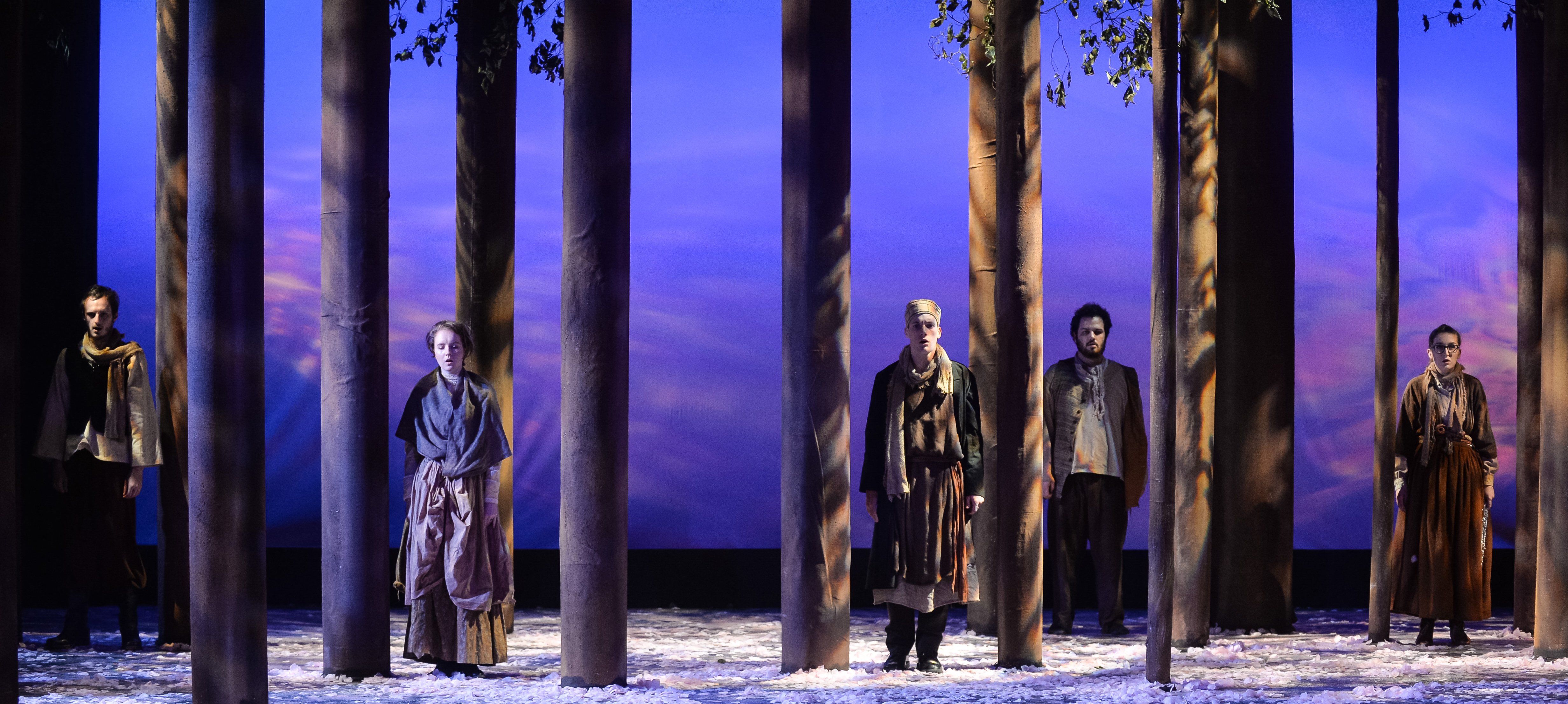 Five ensemble members performing in “The Cherry Orchard” by Anton Checkov. Actors are standing among the set of trees peering at the audience.